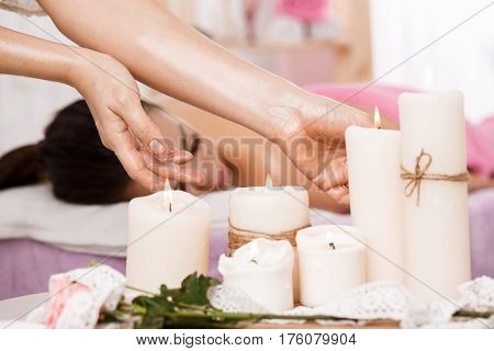 Beauty and body care concept. Young pretty woman on massage couch. Massuer taking candles