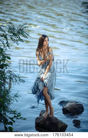 Woman in beach. Girl in blue dress standing alone on rocky stone in water wating for somevone. Fashion Art Photo. Fashion creative shot of one seductive multi-racial Asian Caucasian sexy female.