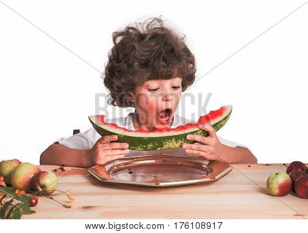 Little curly boy eats large ripe watermelon. Blue background. Close-up.
