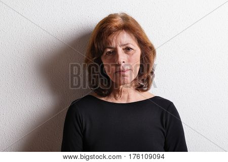 Beautiful senior woman in black t-shirt. Studio shot against white wall.