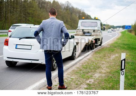 Man calling while tow truck picking up his broken car.