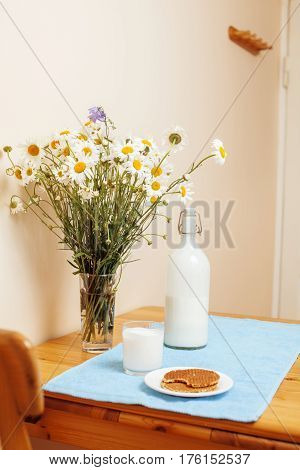 Simply stylish wooden kitchen with bottle of milk and glass on table, summer flowers camomile, healthy foog moring concept noone