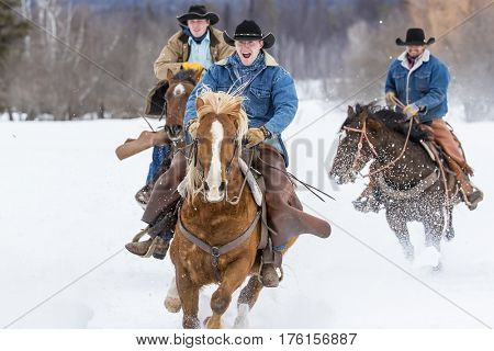 Cowboys round up a herd of horses as they're running through the snow in the mountains