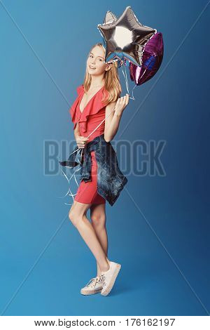 Valentine's Day. Woman in red dress holding balloons on the blue background. Processed with VSCO s3 preset