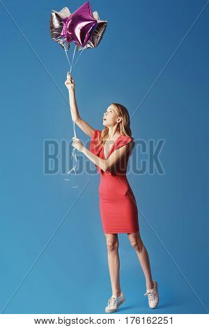 Valentine's Day. Woman in red dress holding balloons on the blue background. Processed with VSCO s3 preset