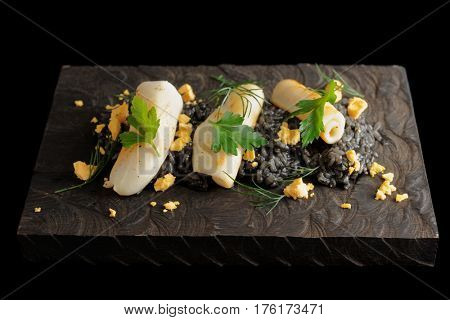 Black risotto with squid ink and seared calamary on wooden board, isolated on black