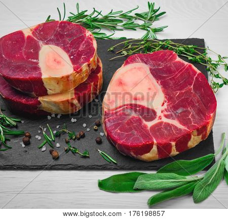 meat beef veal shank slices meat for Osso Buco cooking on white wooden background. Ingredients for beef meat Osso Buco sage leaves thyme rosemary pepper salt pepperl.