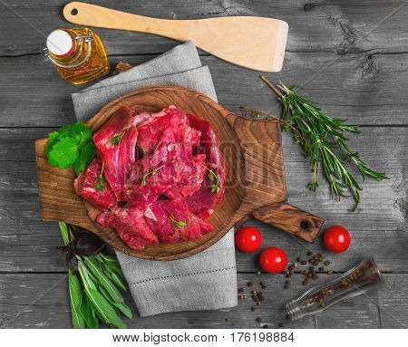 Fresh raw chopped meat beef on an wooden board plate. Raw ingredients spices herbs thyme coriander basil olive oil and vegetables on gray wooden background for raw chopped meat beef. Top view