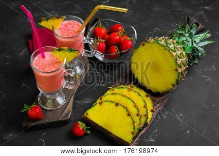 Summer Fruit cocktail smoothie with strawberries and pineapple in the glasses. Ingredients for cocktail smoothie of fresh strawberries and pineapple. Dark black background.