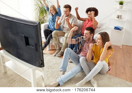friendship, leisure, people and entertainment concept - happy friends with remote control and drinks watching tv at home