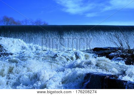 Dam with flowing water. Blue sky on background.