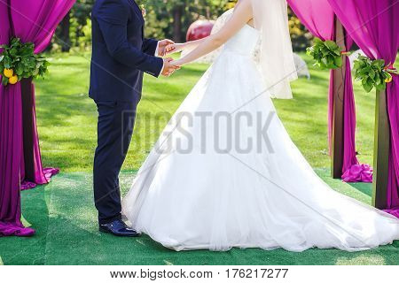 Newlyweds staying arm in arm, under wedding arch, closeup