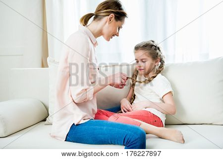 Side View Of Smiling Mother Pleaching Daughter's Hair In Braids