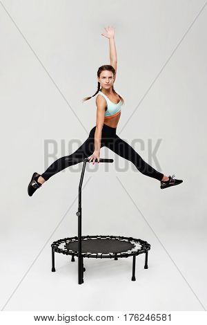 Young sporty woman in blue top and black pants jumping up on rebounder looking straight