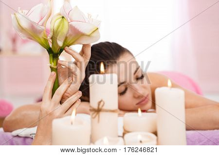 Woman relaxing at spa in bright room with lighted candles and tender flowers. Good vibes