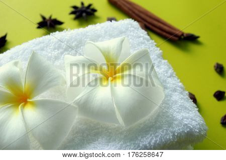 White towel with flowers of plumeria with stars of anise and cinnamon sticks on the yellow background for spa theme.