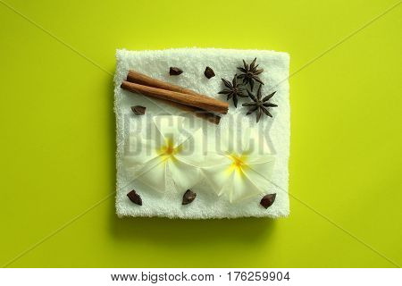White towel with flowers of plumeria with stars of anise and cinnamon sticks on the yellow background for spa theme.
