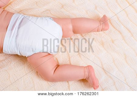 feet of a six months old baby wearing diapers lying in bed at home