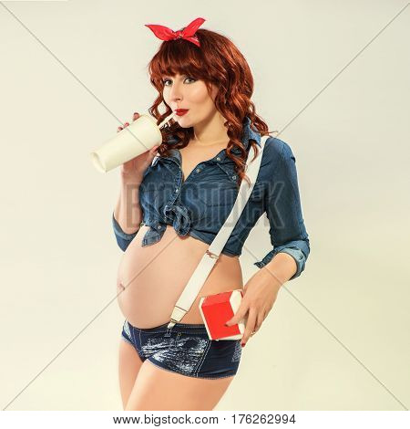 Fashionable redhead pregnant woman in pin up style drinking cold drink and hold burger box