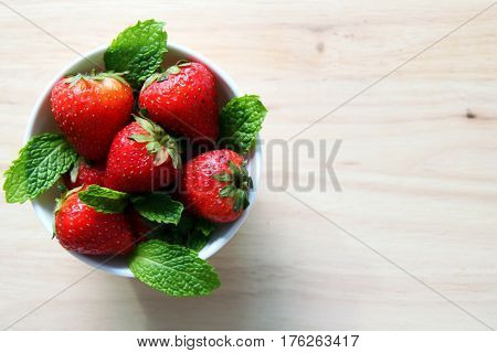Fresh strawberry with leaves of mint on the wooden background.