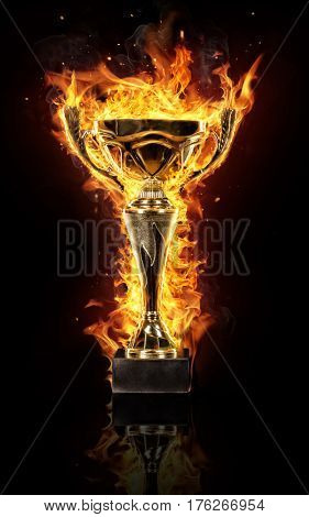 Burning gold trophy cup isolated on black background, flames around. Concept of success and effort.