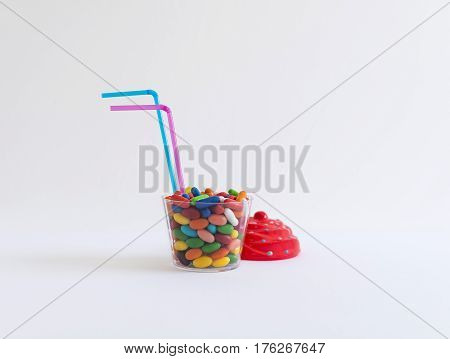 Transparent plastic cup with colorful candy with two blue and pink colored straws on white background.