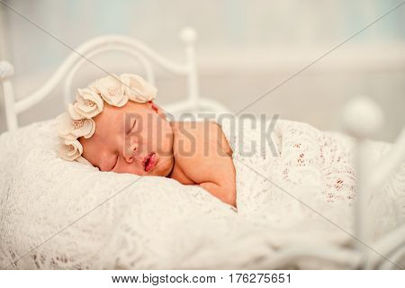 Newborn girl sleeping on the tummy to decorative crib. Portrait of a sleeping newborn girl with floral bandage on his head covered with delicate tippet. Horizontal