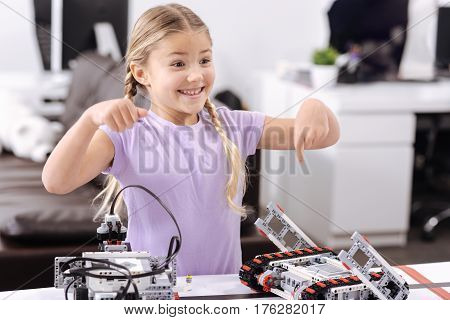 Look at this robot. Joyful smiling optimistic girl standing at school and demonstrating cyber robot while expressing positivity