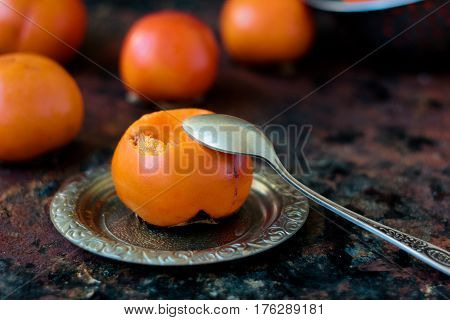 Someon Start To Eat Persimmon On Siver Plate Over Rustic Surface.