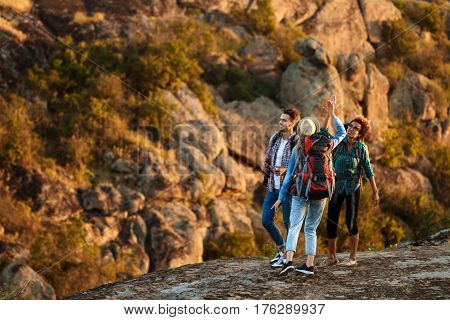 Young cheerful travelers with backpacks smiling, giving highfive, walking in canyon. Copy space.