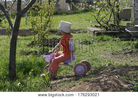 Cute girl playing outdoors with a bike and an old bucket helmet