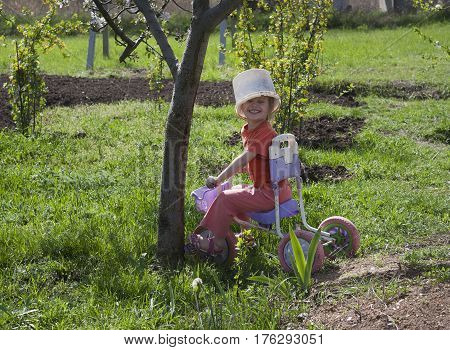 Cute girl playing outdoors with a bike and an old bucket helmet