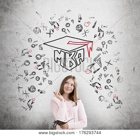 Portrait of a young girl with a notebook standing near a concrete wall with a black and red MBA sketch on it.