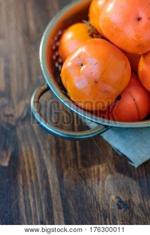 Persimmons In Metal Collander On Wooden Table.