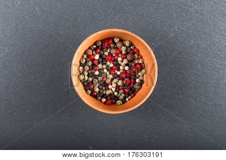 multicolored peppers peas in a clay cup on a slate board top view