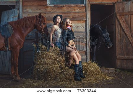 Two women sit on a straw on a farm the horses stand beside them.