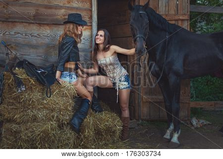 Two female cowboys on a farm with horses sitting on a straw.