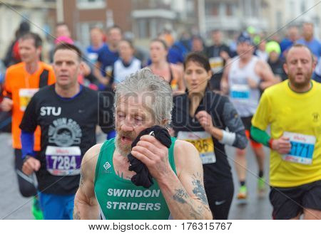 BRIGHTON GREAT BRITAIN - FEB 26 2017: Senior man with beard and competitors r running in the Vitality Brighton half marathon competition. February 26 2017 in Brighton Great Britain