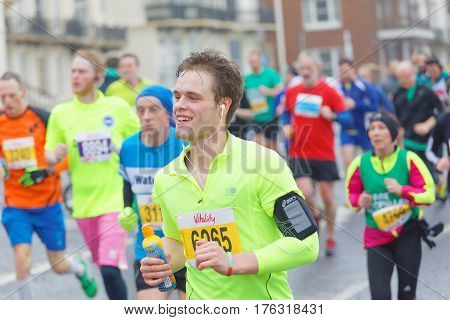 BRIGHTON GREAT BRITAIN - FEB 26 2017: Young smiling man and competitors running in the Vitality Brighton half marathon competition. February 26 2017 in Brighton Great Britain