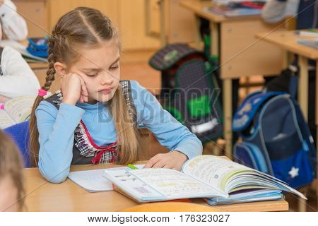 A Girl Pupil In The Classroom At School Looking At A Textbook