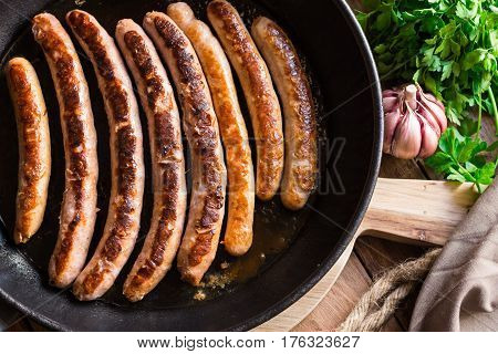 Fried sausages in iron cast pan delicious golden crust garlic parsley wood kitchen table top view