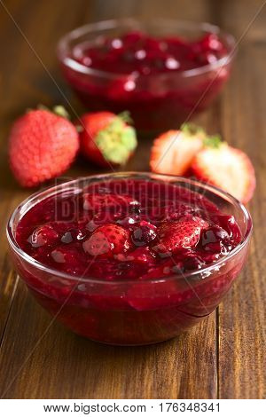 German Rote Gruetze (red groats) red berry pudding made of strawberry blueberry raspberry and redcurrants cooked with sugar and starch photographed on wood with natural light (Selective Focus Focus one third into the first dessert)