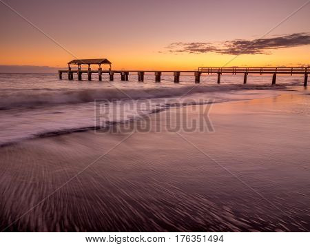 Waimea Town pier at sunset taken with long exposure used to smooth and blur the ocean.
