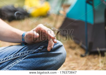 Smoke floats from the end of a joint being smoked at an outdoor camping event.