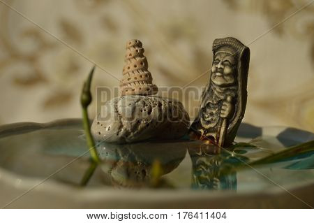 The statue is reflected in the water with a bud of the water lily. Blurred background