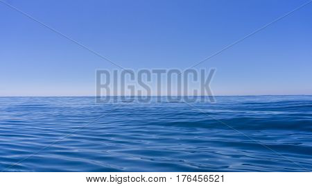 Abstract background deep blue oily looking surface of ocean in motion defocused with hazy sea shimmer and sky on horizon