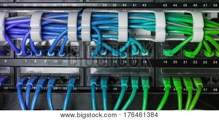 Server rack with blue internet patch cord cables connected to black patch panel in server room horizontal gradient