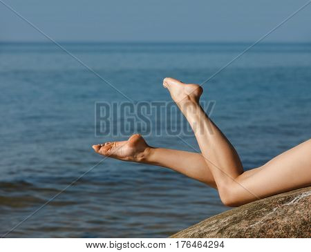 Legs of young nude women lying on stones against the sea background. Naked girl outdoors enjoying nature. Summer paradise. Free Happy Woman