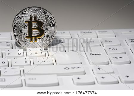 Shining silver and gold metal BTC bitcoin coin on white computer keyboard.