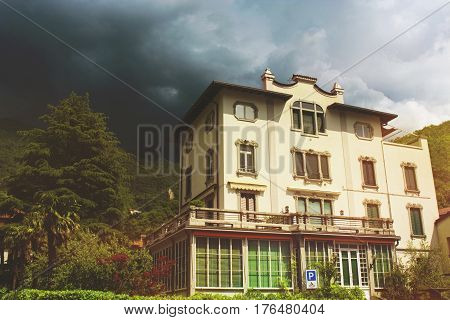 Beautiful toned cityscape of italian Varenna city with building green mountain trees and dramatic cloudy sky before the rain
